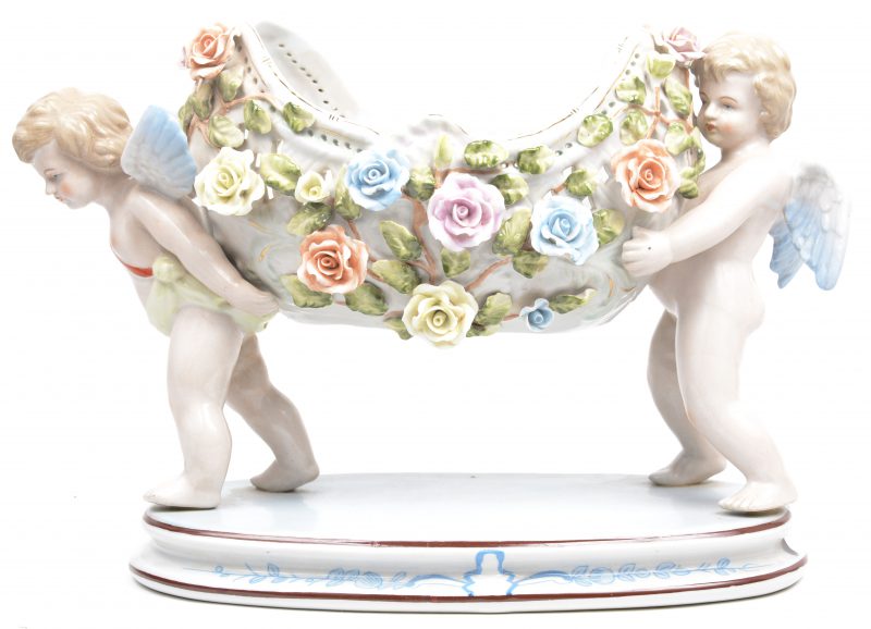 Een jardinière van meerkleurig porselein. in de vorm van een coupe met bloemen, gedragen door twee engelen. Achteraan gemerkt ‘R.B’.