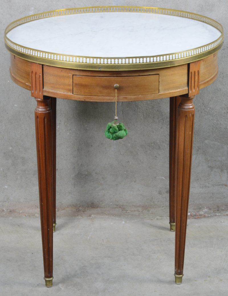Ronde table de milieu met wit marmeren blad, koperen galerij en tapse, gerainureerde poten. In de gordel twee laden en een schuiftabletje. Lodewijk XVI-stijl.