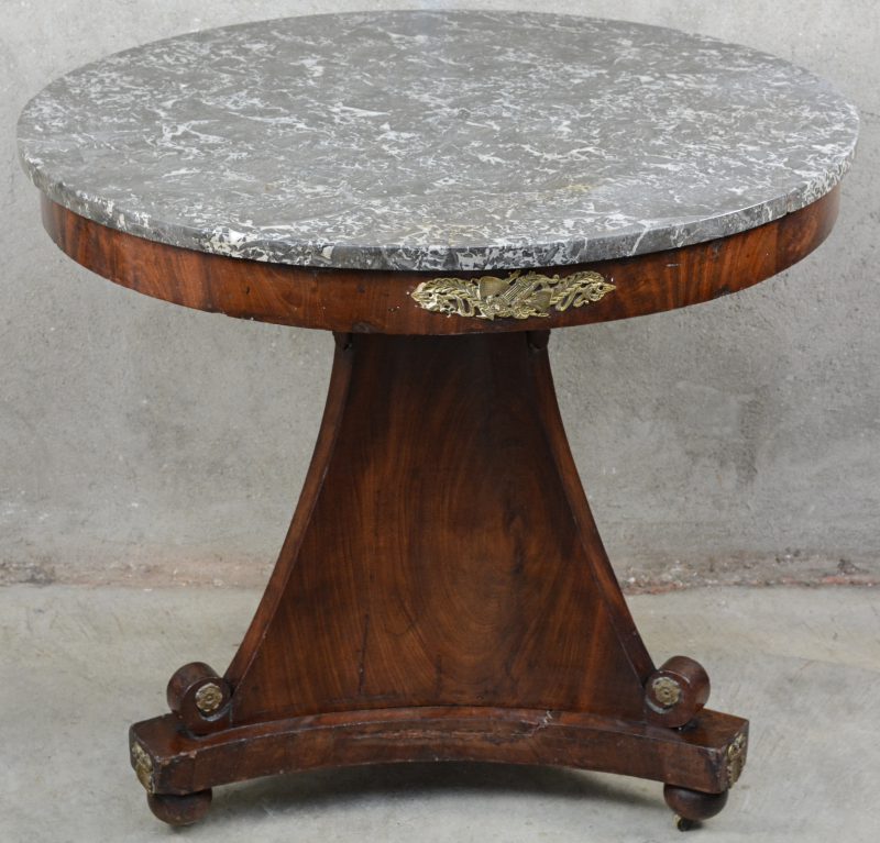 Een ronde gefineerde mahoniehouten Empire tafel op driepoot met grijs marmeren blad. Verguld koperen monturen op de voet. Op te frissen.