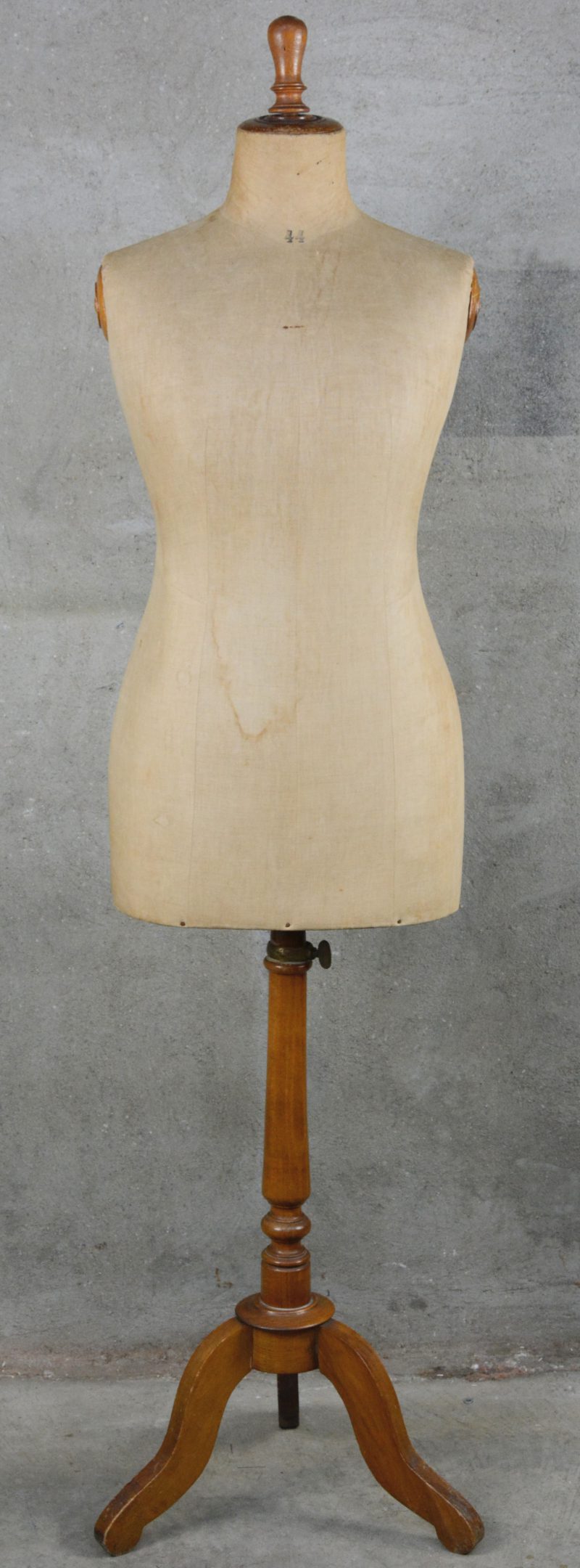 Een oude met linnen beklede paspop op houten voet.