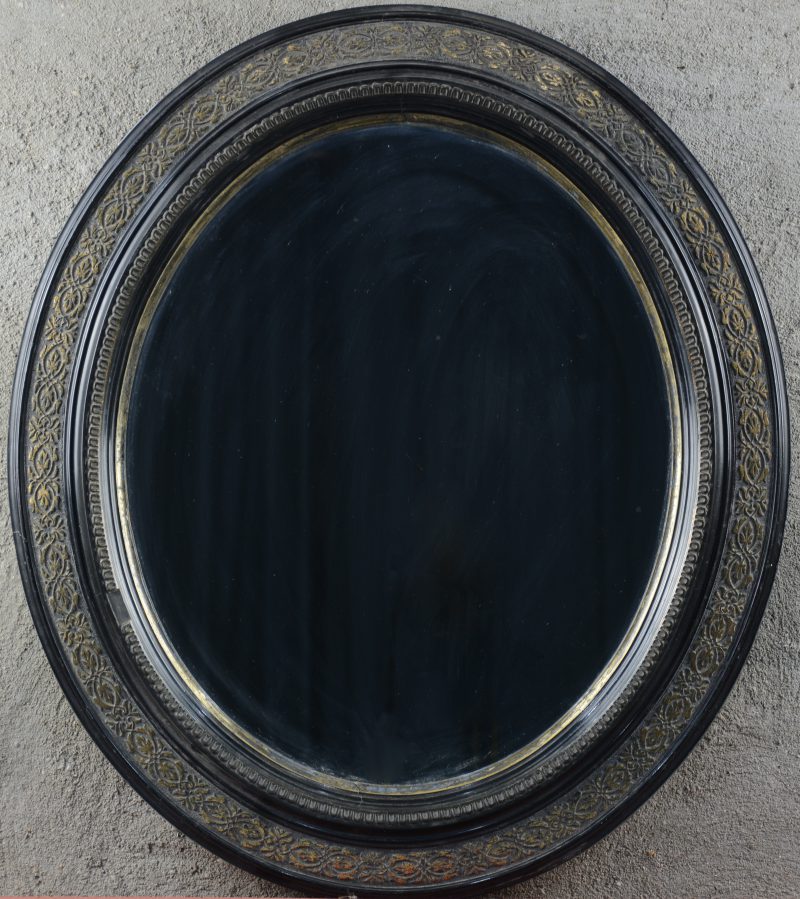 Een ovale spiegel met houten lijst, versierd met vergulde motieven.