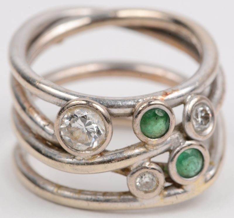 Een 18 karaats wit gouden ring bezet met briljanten met een gezamenlijk gewicht van +- 0,40 ct. en twee smaragden met een gezamenlijk gewicht van +- 0,20 ct.