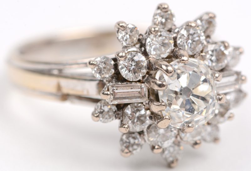 Een 18 karaats wit gouden bloemvormige ring bezet met briljanten en diamant baguetten met een gezamenlijk gewicht van +- 0,70 ct. en een centrale briljant cushion shape van +- 1,03 ct.
