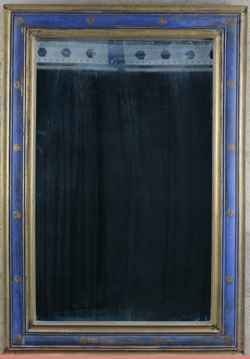 Een rechthoekige spiegel van deels blauwgepatineerd en met messing beslagen hout.