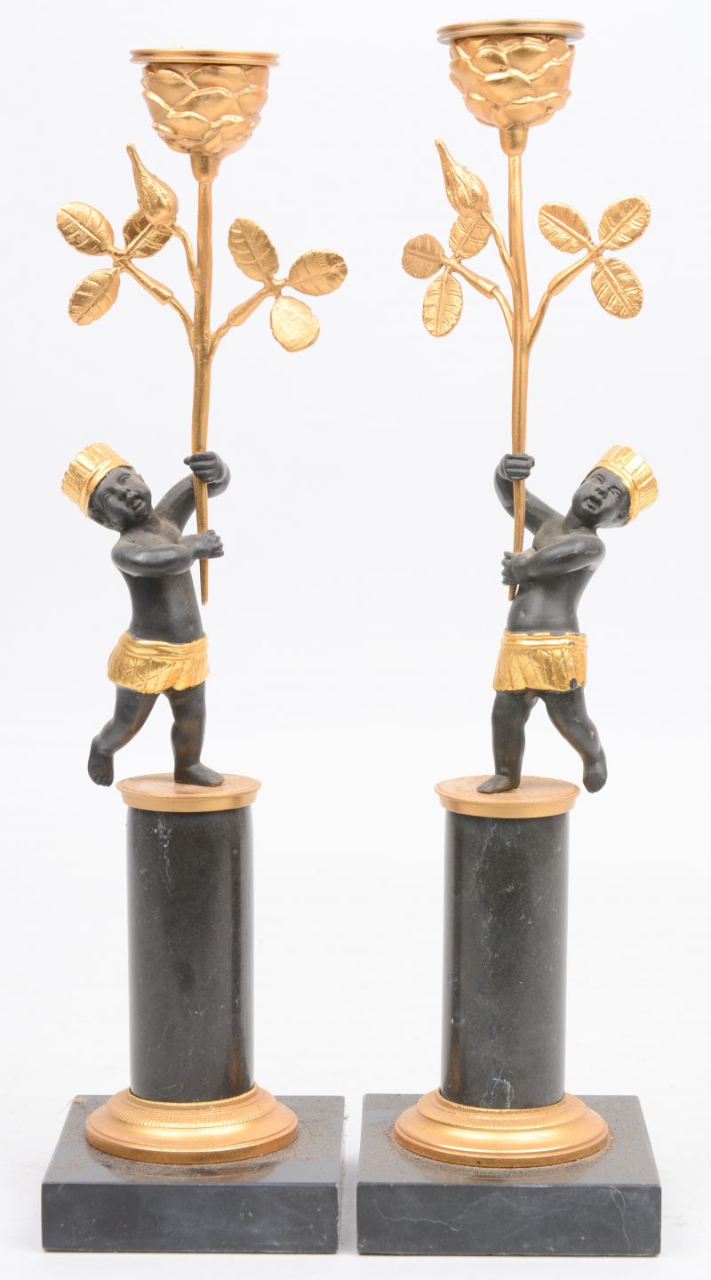 Een paar vergulde kandelaars, gedragen door bronzen moriaantjes op een marmeren zuiltje.