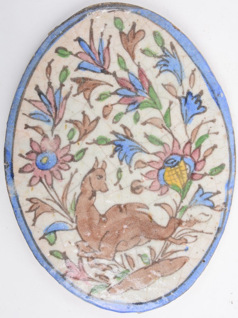 Een ovale plaquette van Perzisch aardewerk met een meerkleurig decor van een hinde en bloemen.