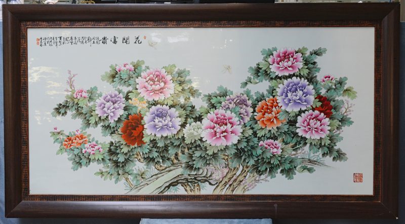 Een grote plaquette van Chinees porselein met meerkleurig decor van een bloeiende pioenenstruik en vlinders. Gemerkt.