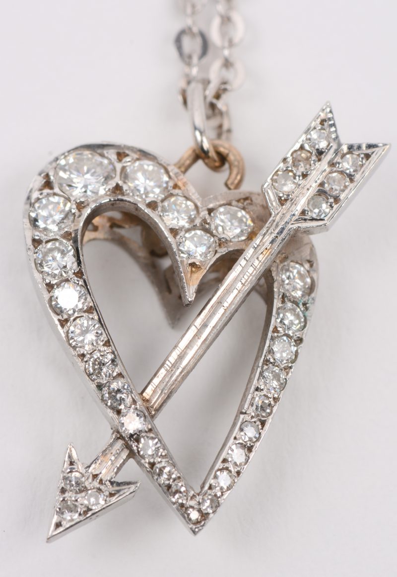Een 18 karaats wit gouden ketting met hanger in de vorm van een hart met pijl bezet met een briljanten met een gezamenlijk gewicht van +- 0,60 ct.