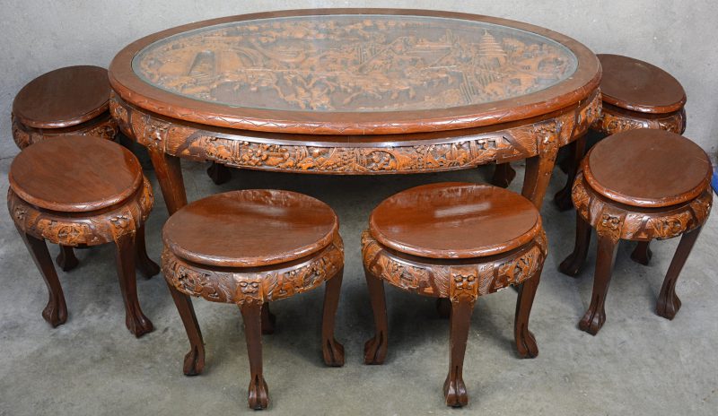 Een lage ovale Chinese tafel, versierd met een gesculpteerd decor van krijgers onder glas. et zes krukjes.