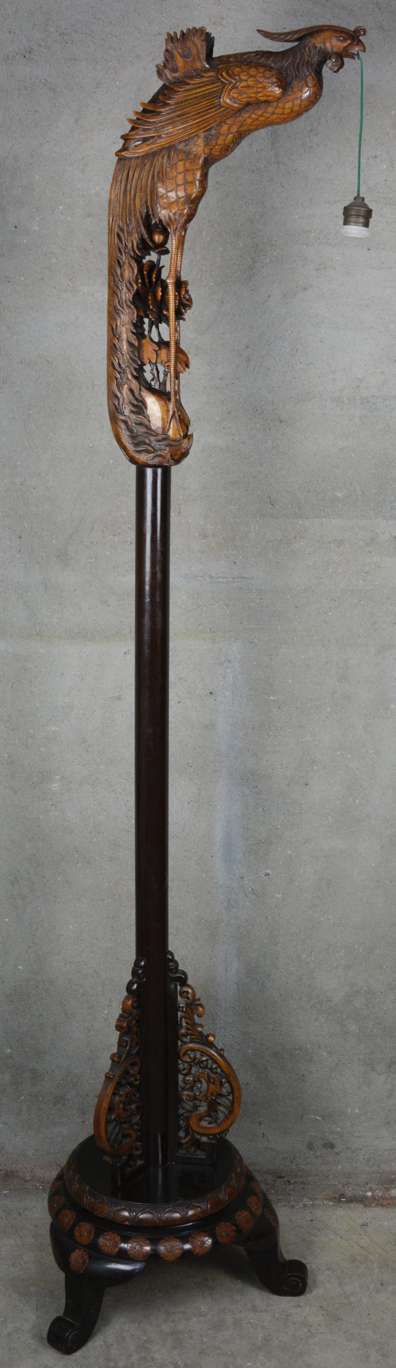Een gebeeldhouwd houten Chinese staande lamp met hanglampion, gedragen door een feniks.