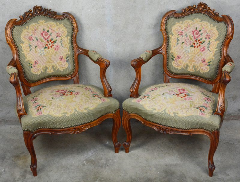 Een paar Lodewijk XV fauteuils van gebeeldhouwd notenhout bekleed met naaldwerk.