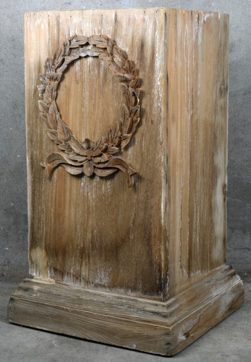 Een houten presentatiesokkel, versierd met een uitgestoken lauwerkrans.