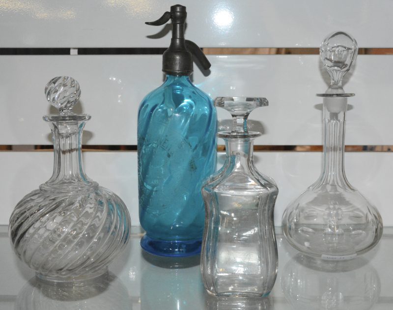 Een lot van drie karaffen, waarbij één kristalklen en twee glazen (twee doppen onderaan beschadigd) en een oude Engelse sodafles van blauw glas.