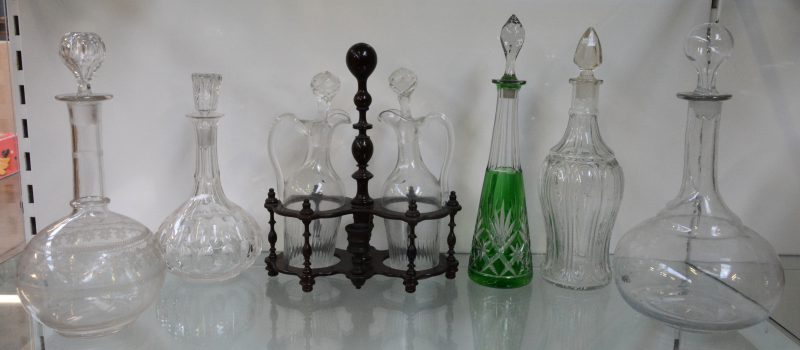 Een lot glaswerk, bestaande  uit vier verschillende kleurloze glazen karaffen, een kristallen karaf met groen decor en een glazen olie- en azijnstelltje in houten rekje.