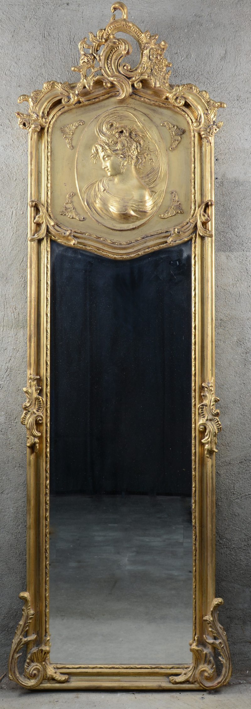 Een verguld houten spiegel in Lodewijk XV-stijl, versierd met een vrouwenprofiel in reliëf.
