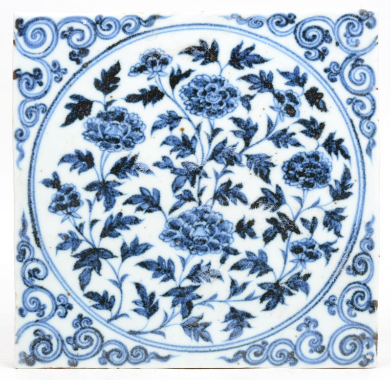 Een tegel van Chinees porselein met een blauw op wit decor van pioenen.