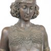 “Vrouw in klederdracht van de jaren ‘20, leunend tegen muurtje met sfinxen”. Een grope van brons en wit marmer. Marmer gerestaureerd.