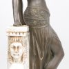 “Vrouw in klederdracht van de jaren ‘20, leunend tegen muurtje met sfinxen”. Een grope van brons en wit marmer. Marmer gerestaureerd.
