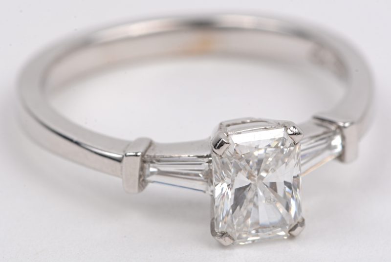 Een 18 karaats wit gouden ring bezet met een diamant emerald cut van +- 0,90 ct. FSI1. en twee diamant baguetten met een gezamenlijk gewicht van +- 0,20 ct.
