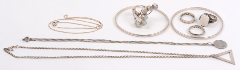 Een lot zilveren juwelen waaronder drie kettingen waarvan twee met hangers, vier ringen waarvan twee met half edelstenen en twee slavenarmbandjes.