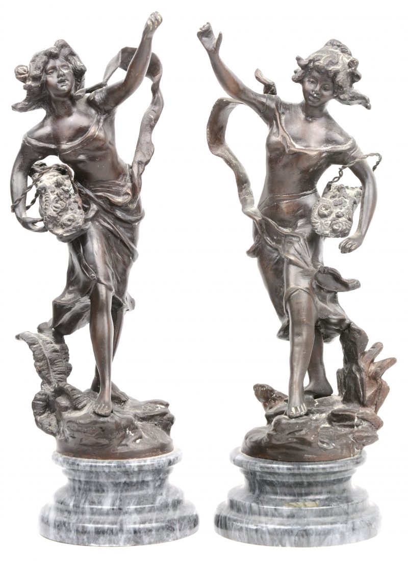 “Vrouwen met bloemenmanden”. Een paar bronzen beelden naar werk van Moreau. Op grijs marmeren sokkels.
