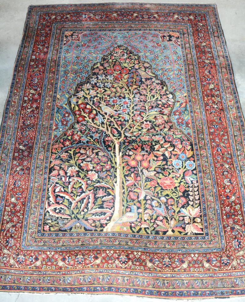 Een handgeknoopt Perzisch tapijt met een levensboom in het decor.