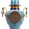 Een driedelig klokstel van koper en porselein met een blauw decor van korenbloemen. Begin XXste eeuw. Met sleutels en slinger.