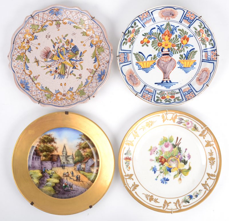 Vier borden, waarvan een polychroom Delfts, een polychroom Rouens, een porseleinen bord met landschapsdecor en vergulde rand en een Frans porseleinen bord met bloementuil en vergulding. XIXde en XXste eeuw.