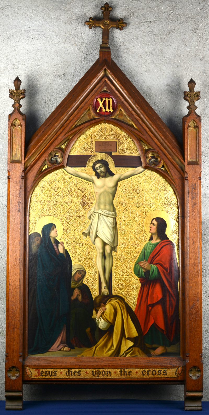 “Jesus dies upon the cross”. Een onderdeel van de kruisweg met olieverf en goudverf in gebeeldhouwde kader.