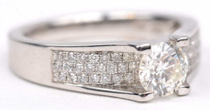 Een witgouden ring 18 K bezet met een centrale diamant van +- 0,76 ct. GVS2 en briljanten met een gezamenlijk gewicht van +- 0,32 ct.