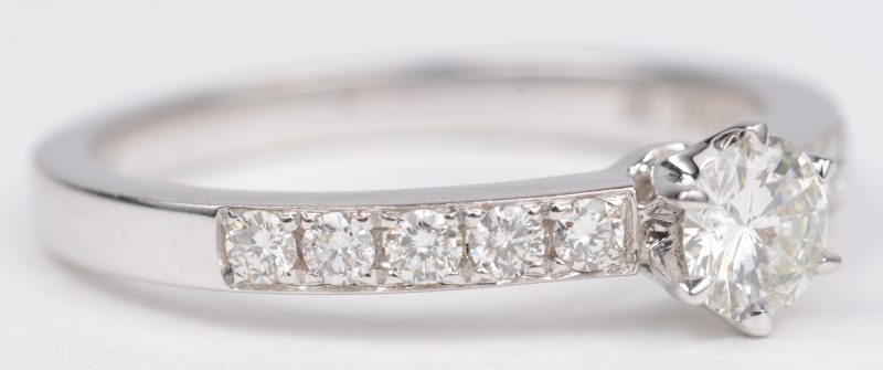 Een 18 K witgouden ring bezet met een centrale briljant van +- 0,25 ct. en  met briljanten een gezamenlijk gewicht van +- 0,20 ct.