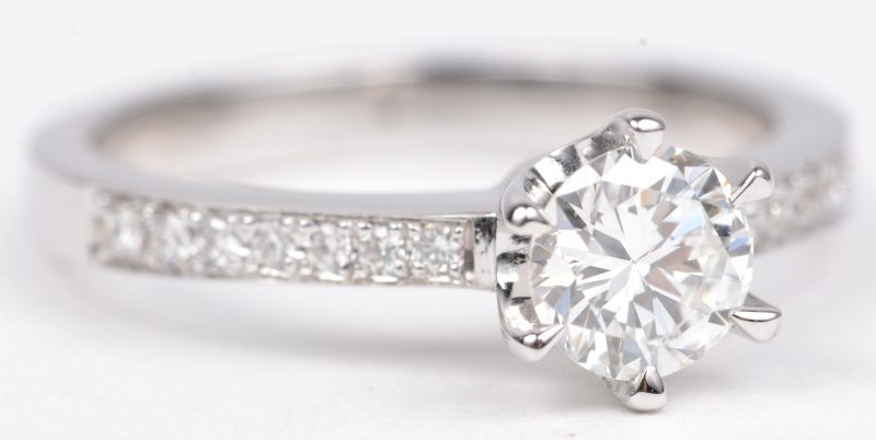 Een 18 K witgouden ring bezet met een centrale briljant van +- 0,60 ct. FVS2 en briljanten een gezamenlijk gewicht van +- 0,14 ct.