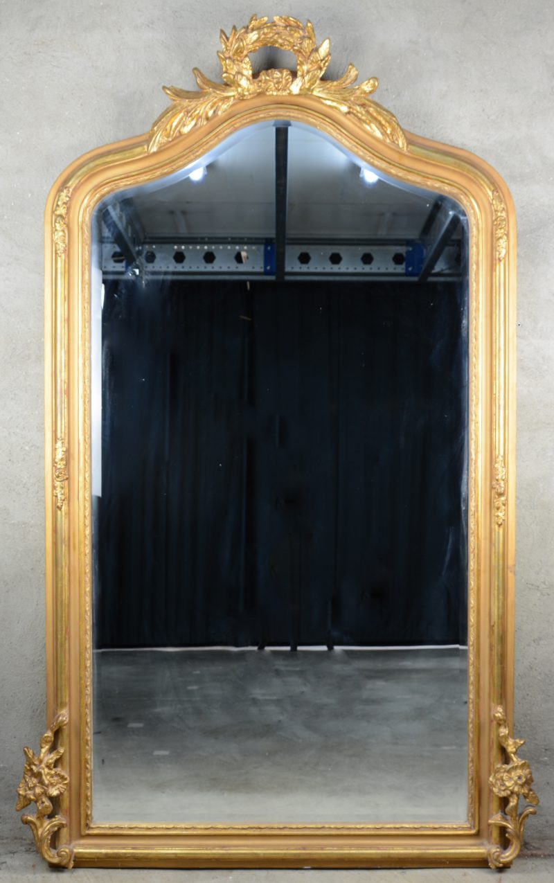 Een verguld houten schouwspiegel, bovenaan getooid met een lauwerkrans en aan de zijkanten met bloementuilen.