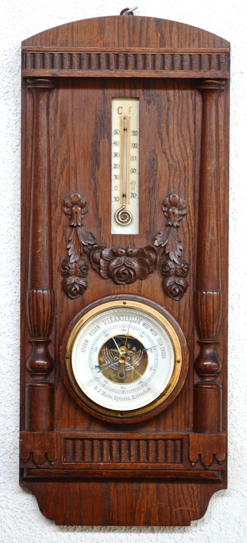 Een eikenhouten barometer-thermometer met gesculpteerde versieringen. Glas gebarsten.
