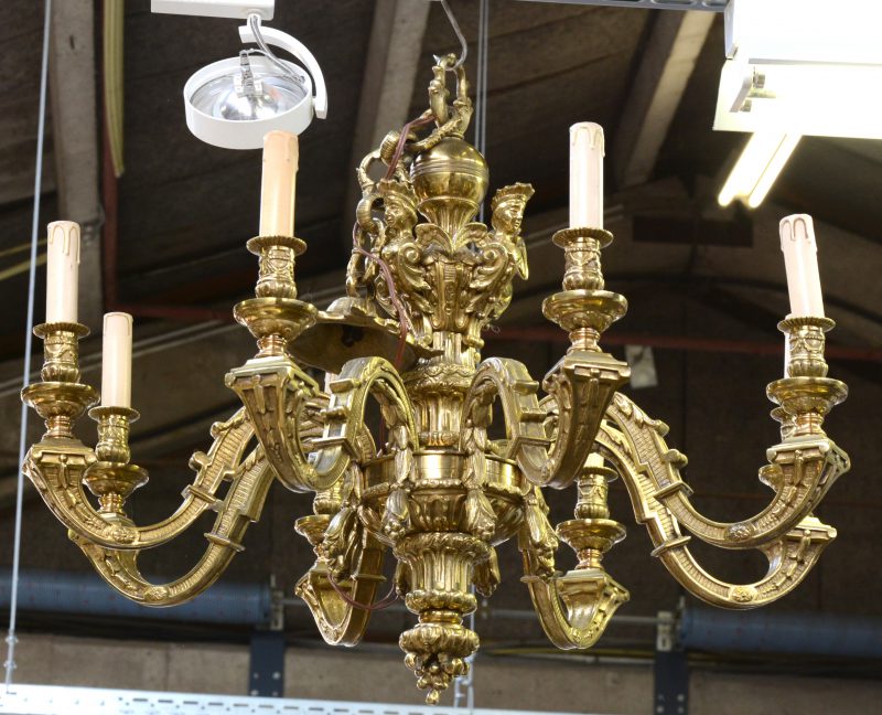 Een verguld bronzen mazarinluchter met acht lichtarmen, bovenaan versierd met hermenfiguren.