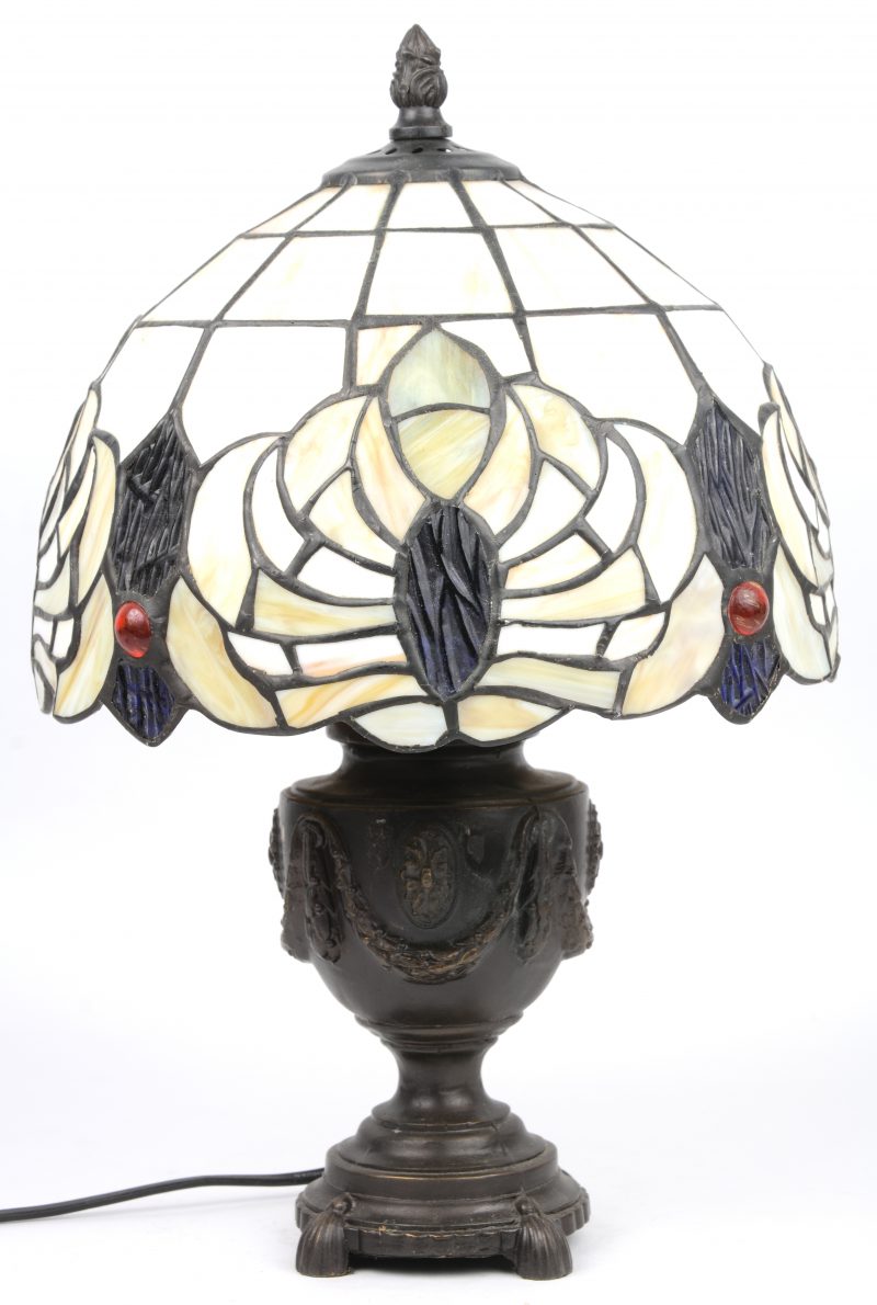 Een bronzen lampje met voet in de vorm van een empire siervaas en met kap van glas in lood.