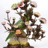 Een kandelaar met twee lichtpunten, uit brons opgebouwd in de vorm plantenranken met porseleinen bloemen rond een centrale papegaai en op bronzen voet in barokke stijl. Onderaan gemerkt.