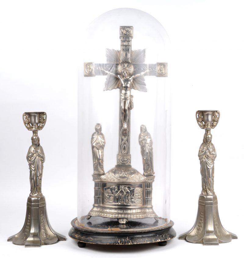 Een verzilverd kruisbeeld met twee kandelaars en glazen stolp.