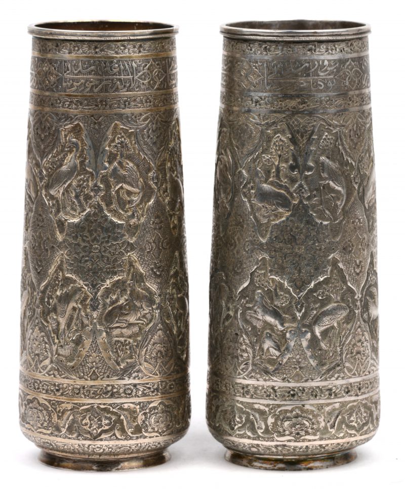 Een paar lichtjes vernauwende cylindrische vaasjes van gedreven en geciseleerd zilver versierd met vogels en dieren in uitsparingen. Perzië, Qadjar, begin XXste eeuw. Onderaan gemerkt: 840/1000.