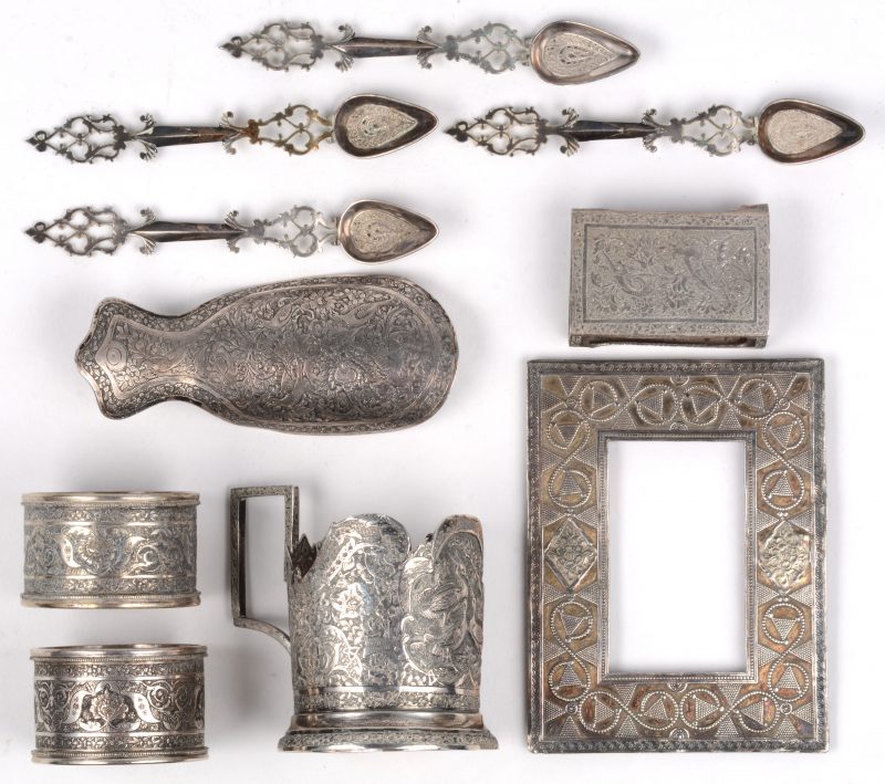 Een lot kleine geciseleerde zilveren voorwerpen: een theeglashouder, twee servetringen, een fotolijstje, een schoentrekker, een luciferhouder (schade), vier geajoureerde lepeltjes. Iran, begin XXste eeuw.