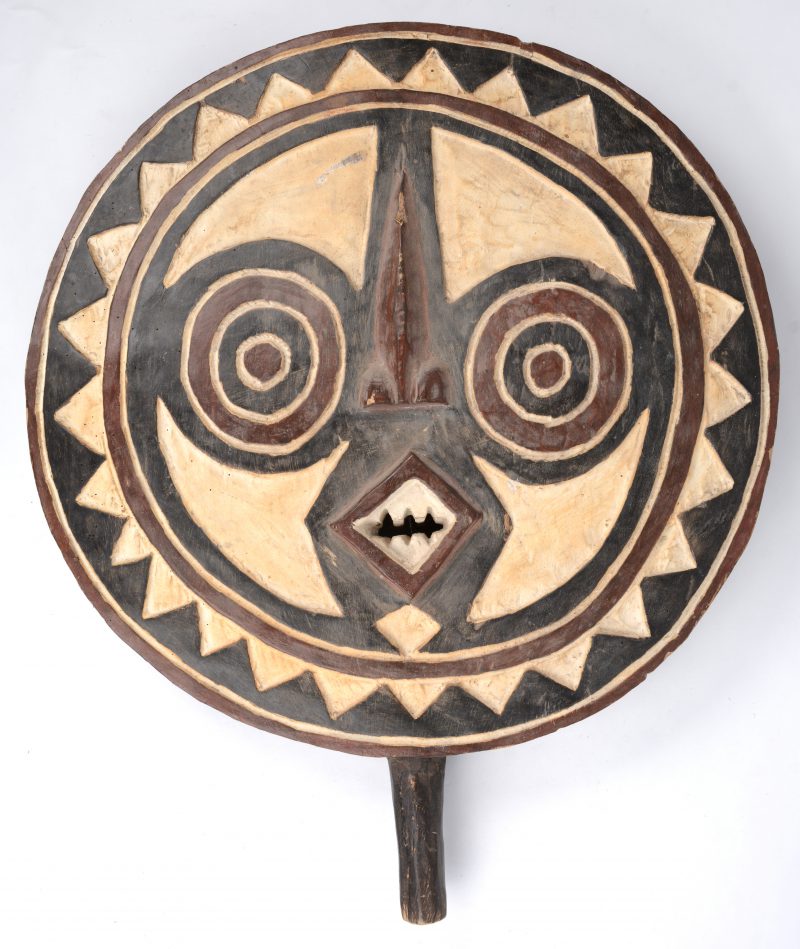 Een rond Afrikaans masker van gebeeldhouwd en gepolychromeerd hout.