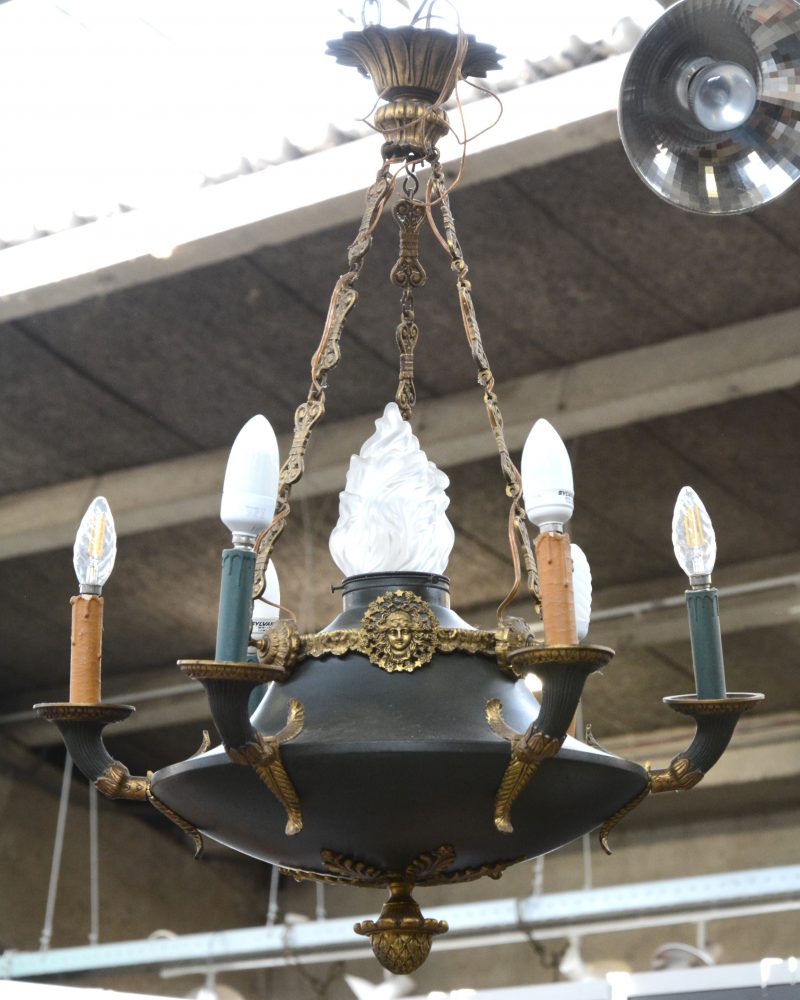 Een Empire halllamp van messing en plaatijzer met centraal een glazen vlam en rondom zes lichtpunten.