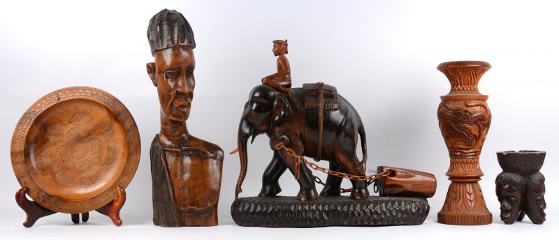Een lot gebeeldhouwde houten voorwerpen en beelden, bestaande uit een Afrikaanse buste, een Afrikaanse asbak met drie hoofden, een Indische bosbouwer op olifant (lichte schade aan de kettingschakels), een siervaas met drakendecor en een sierbord.