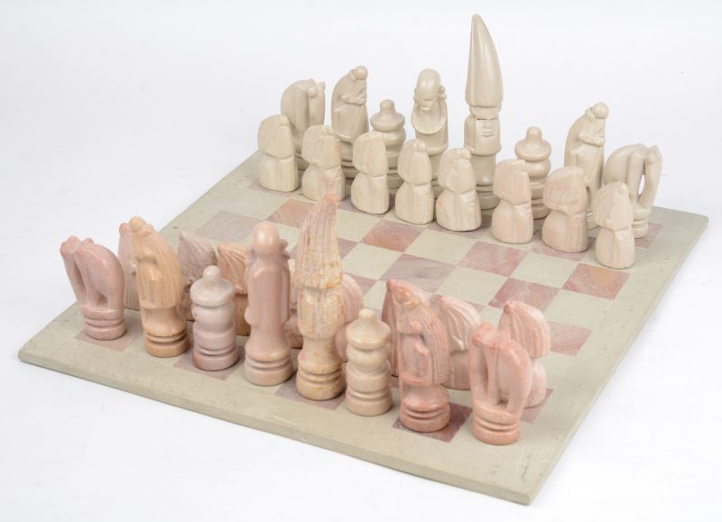 Een schaakspel en bord van gebeeldhouwd natuursteen. Een loper gelijmd. Afrikaans werk.