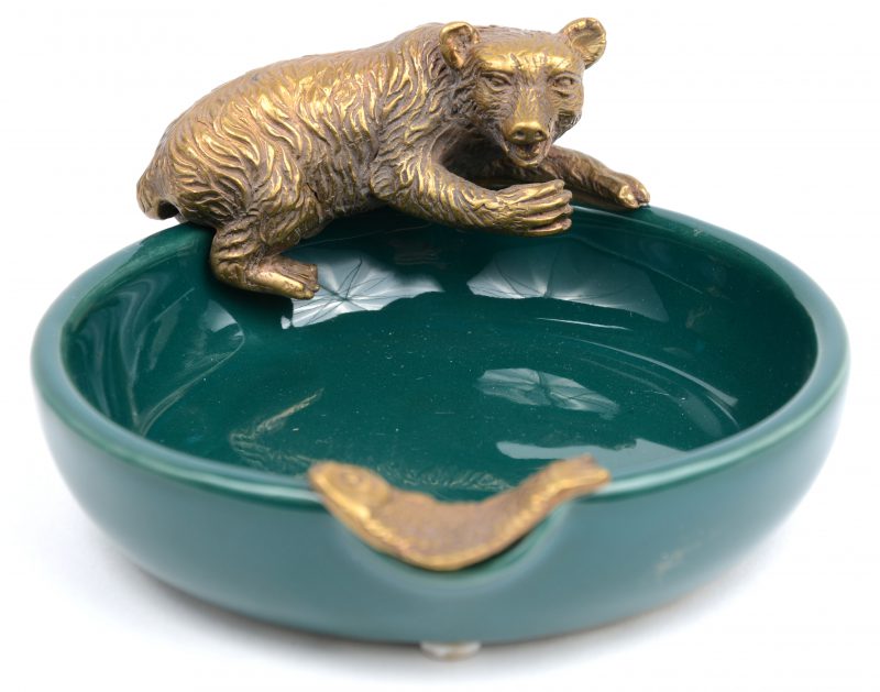 Een asbak van groen geglazuurd aardewerk, versierd met een bronzen beer en vis.