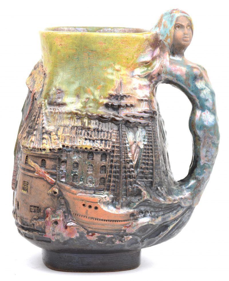 Een terracotta bierpul met meerkleurig geglazuurd reliëfdecor van een havenzicht en het handvat in de vorm van een zeemeermin. Onderaan gemerkt.