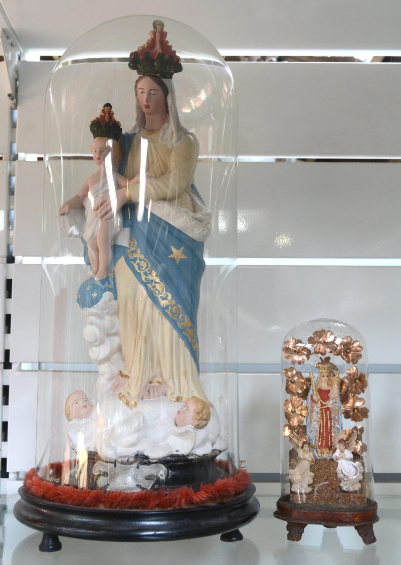 Een grote en een kleine glazen stolp op houten sokkel, waarbij de eerste met plaasteren groep en de tweede met Madonna en kind van was.