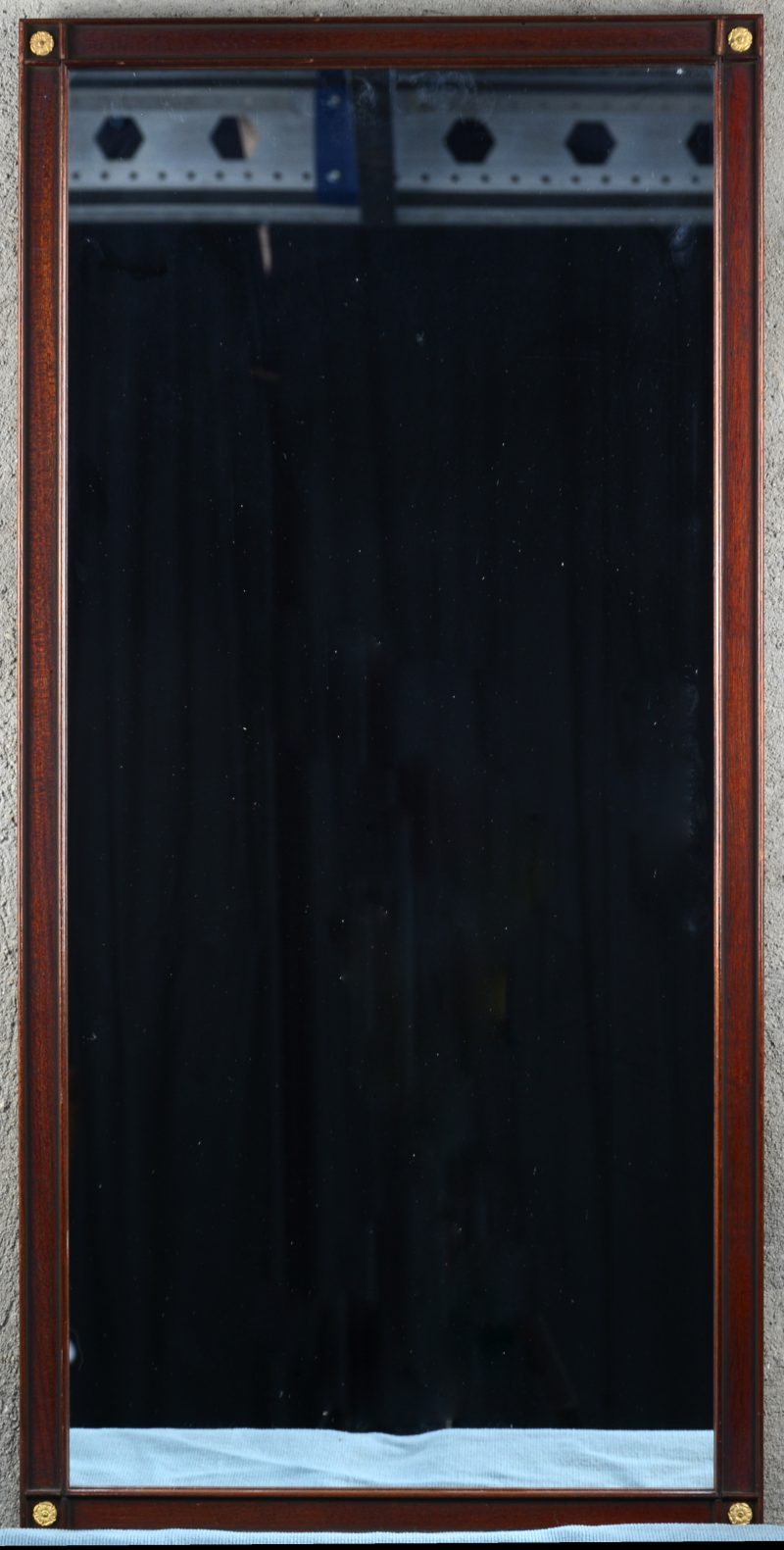 Een rechthoekige spiegel in houten lijst met messingen bloemetjes in de hoeken.