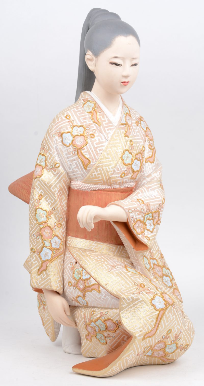 Een knilende geisha van gepolychromeerd gips. Onderaan gemerkt.