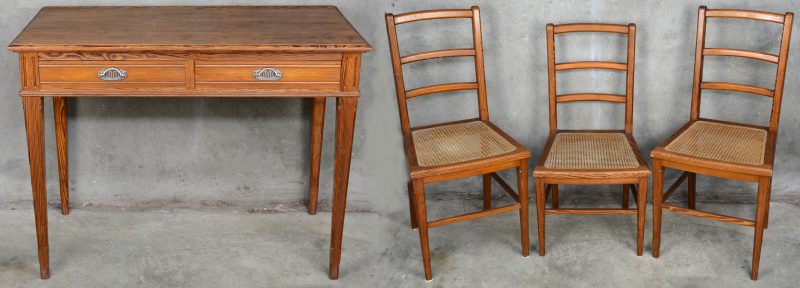 Een sober grenen schrijftafeltje met twee laden en met drie stoelen met gecanneerde zit.
